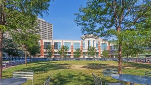 An outdoor courtyard with a central lawn, surrounded by metal tables and chairs, and a building with a mix of brick and glass facade in the background. - Microtel Inn by Wyndham Lexington (Lexington)