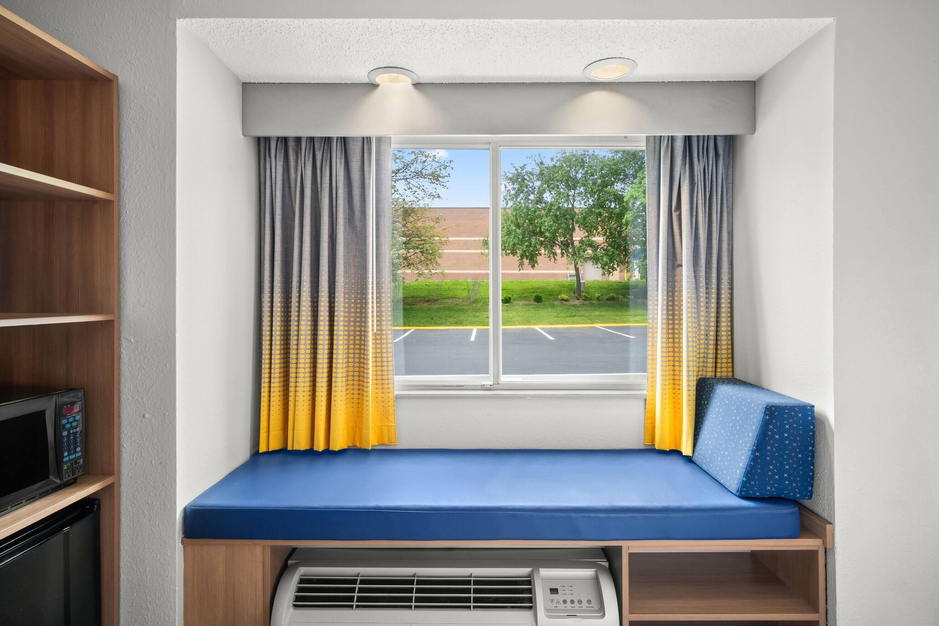 A room with a window, a blue bench, a microwave, and a heater.