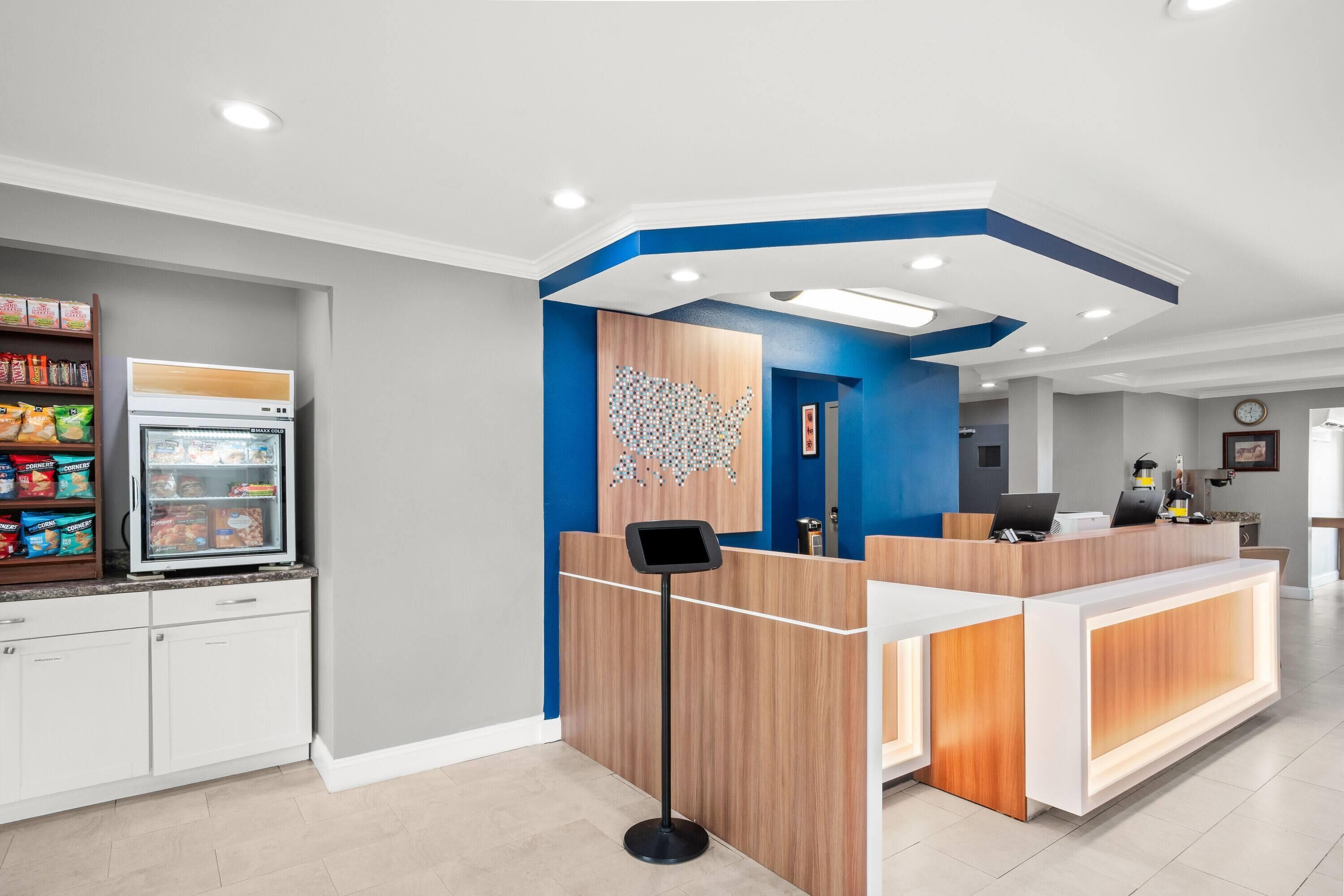 A modern reception area with a wooden reception desk, a digital kiosk, and a refrigerator stocked with snacks.