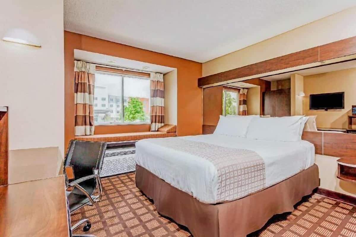 A hotel room with a bed, a desk, a chair, a TV, and a window with curtains.