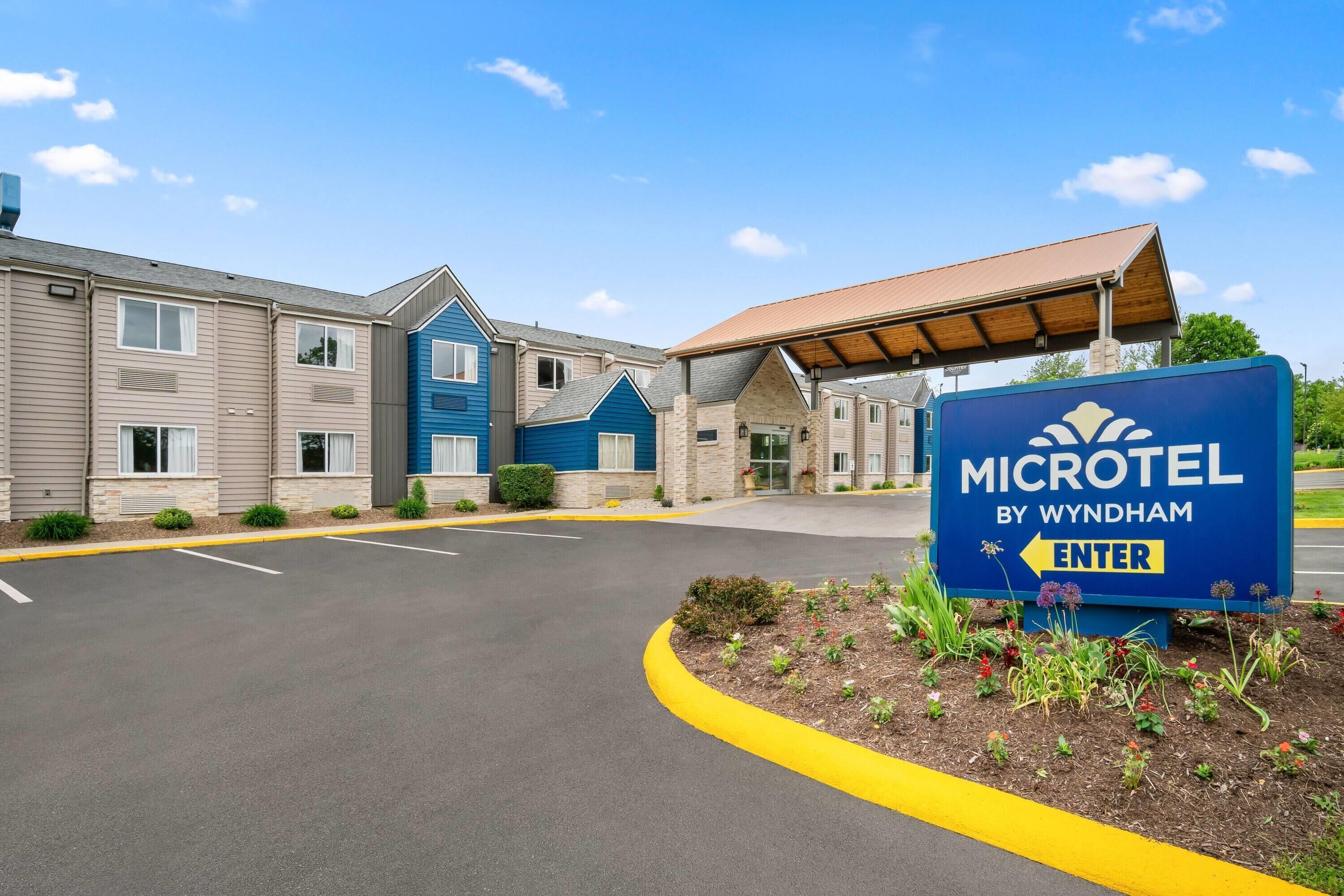 A Microtel by Wyndham hotel entrance with a parking lot and a sign indicating the direction to enter.