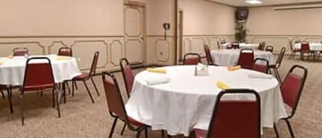 Un salón de conferencias con mesas redondas, sillas rojas y manteles blancos.