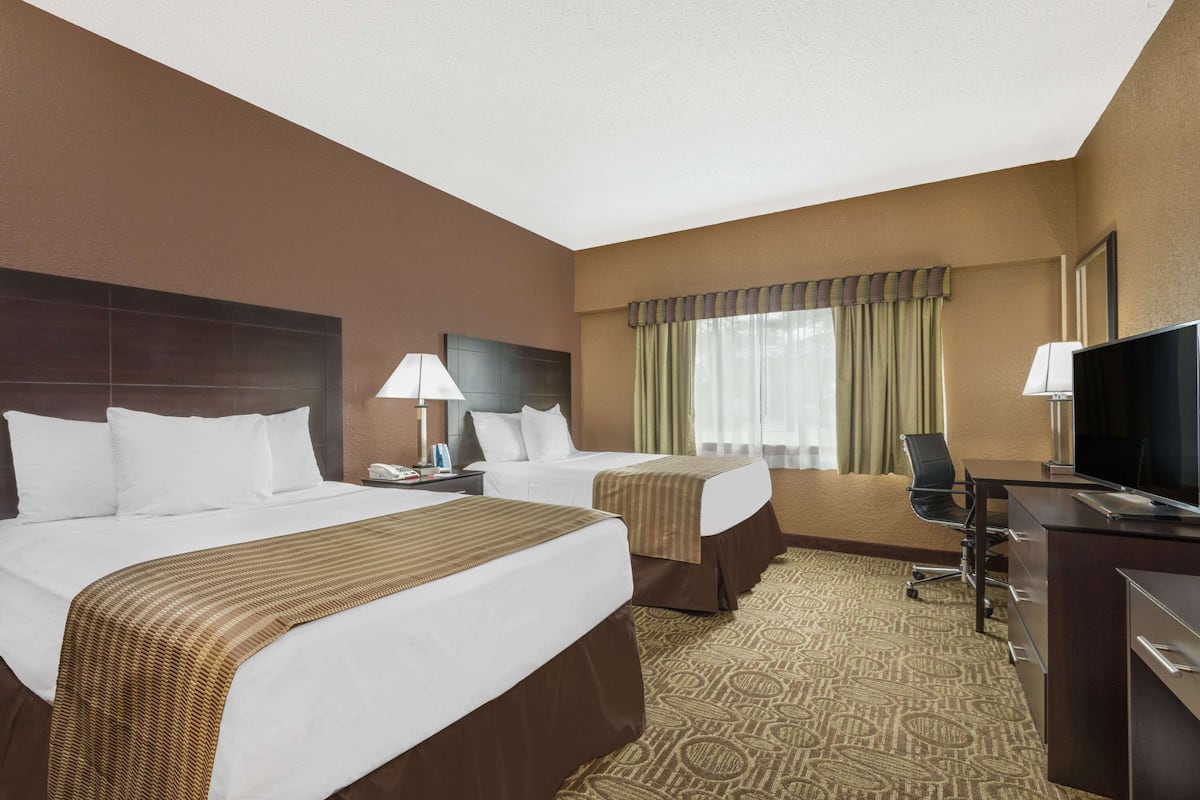 A hotel room with two beds, a desk, a chair, and a television.