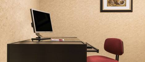A room with a desk, a computer, a red chair, and a framed artwork on the wall.