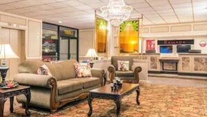 A hotel lobby with a sofa, armchairs, a coffee table, a chandelier, and a reception desk. - Ramada Hotel & Conference Center by Wyndham Paintsville (Paintsville)