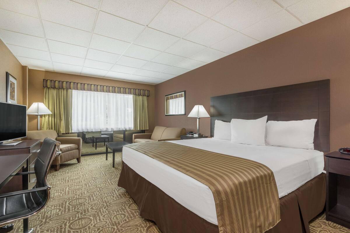A hotel room with a large bed, two chairs, a desk, a television, and a window with curtains.