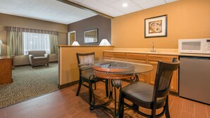 A hotel room with a dining area featuring a glass-top table, two chairs, a sofa, a kitchen area with a microwave, and a refrigerator. - Ramada Hotel & Conference Center by Wyndham Paintsville (Paintsville)