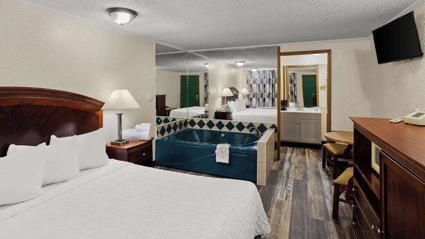 A hotel room with a large bed, a sitting area with a table and chairs, a bathtub, and a desk with a telephone. - Knights Inn Ashland (Ashland)