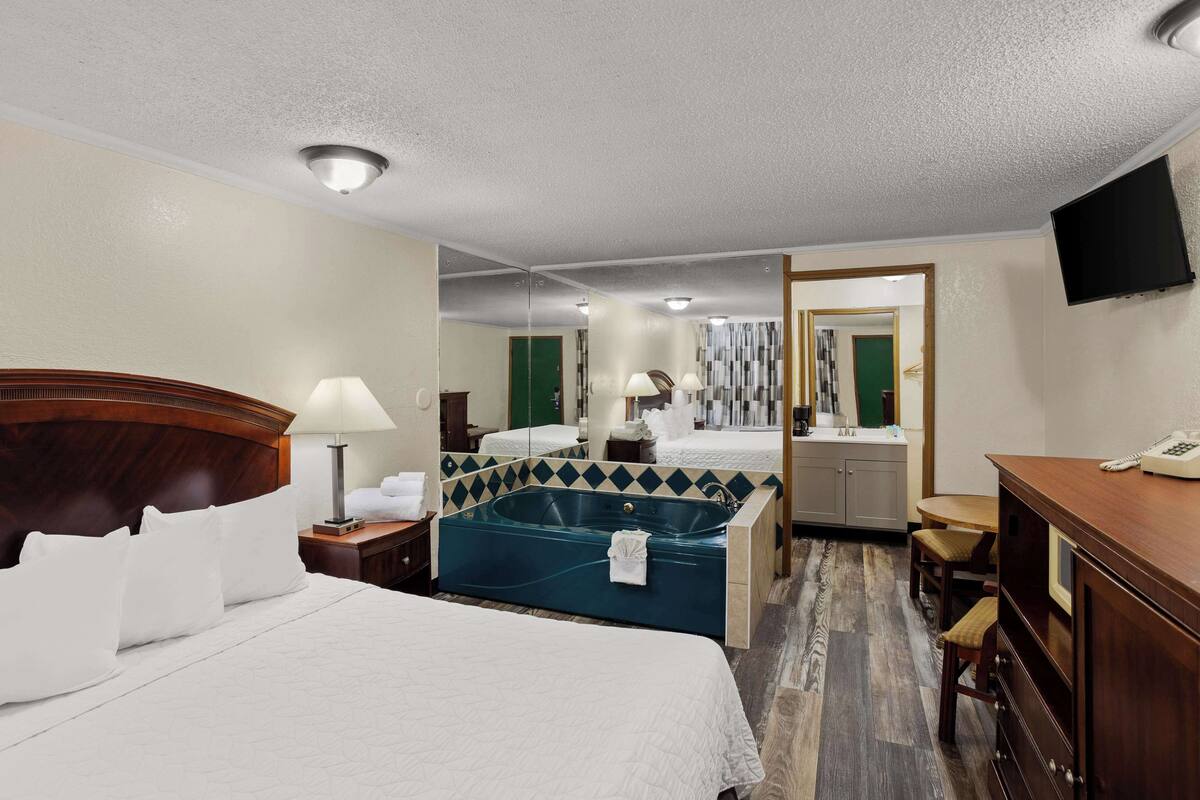A hotel room with a large bed, a sitting area with a table and chairs, a bathtub, and a desk with a telephone.