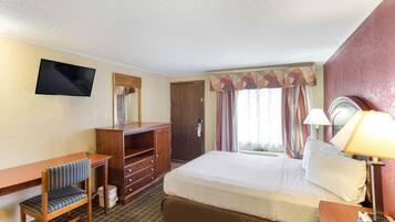 Habitación de hotel con cama, escritorio, silla, televisor, armario y ventana con cortinas.
