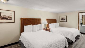 A hotel room with two beds, a nightstand with a lamp, and framed pictures on the walls.