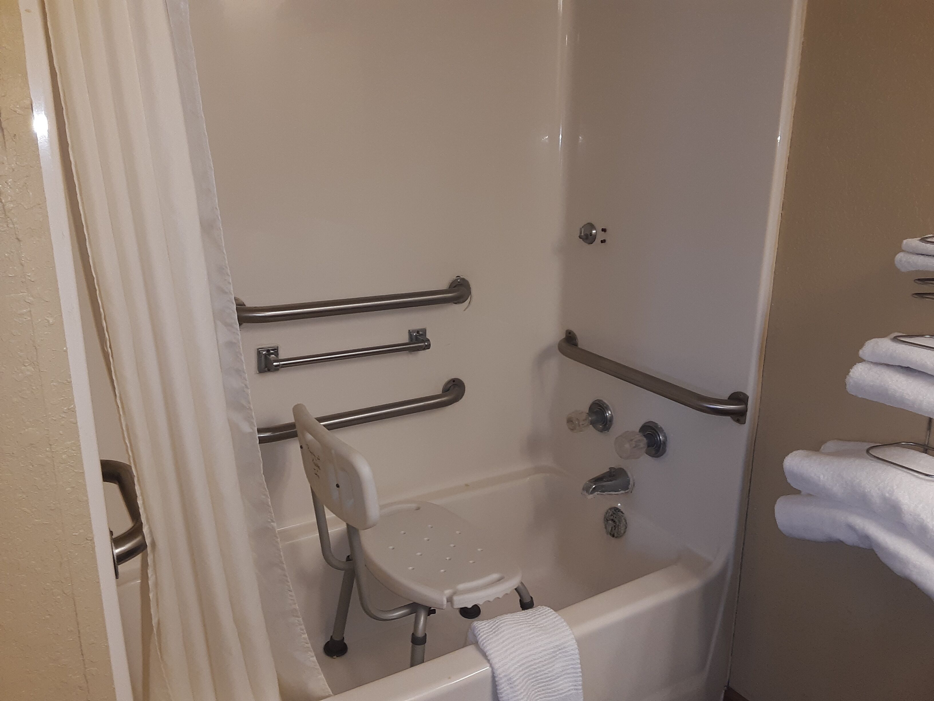 A bathroom with a walk-in shower, grab bars, a handheld showerhead, and a towel rack.