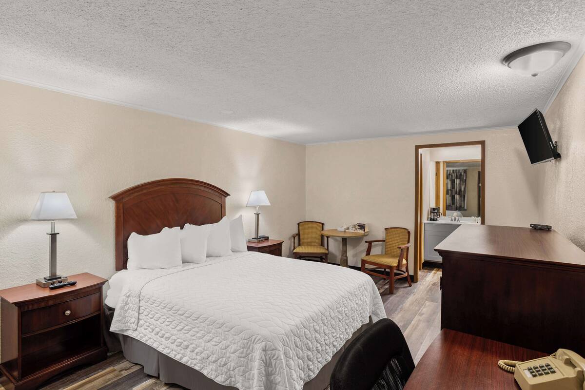 A hotel room with a large bed, two bedside tables with lamps, a desk with a telephone, and two chairs.