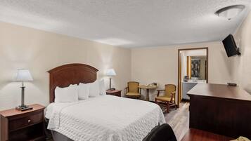 A hotel room with a large bed, two bedside tables with lamps, a desk with a telephone, and two chairs.