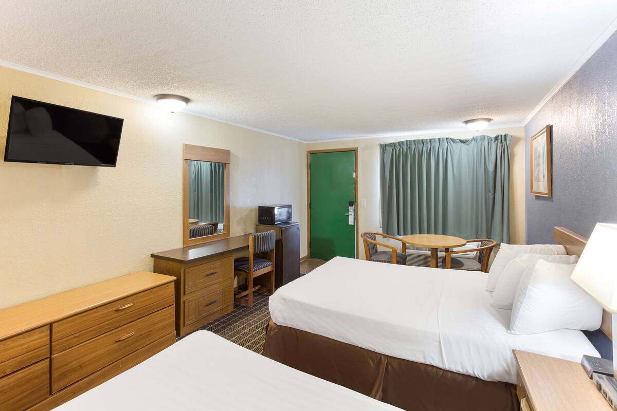 A hotel room with two beds, a desk with a computer, a TV, and a green door.