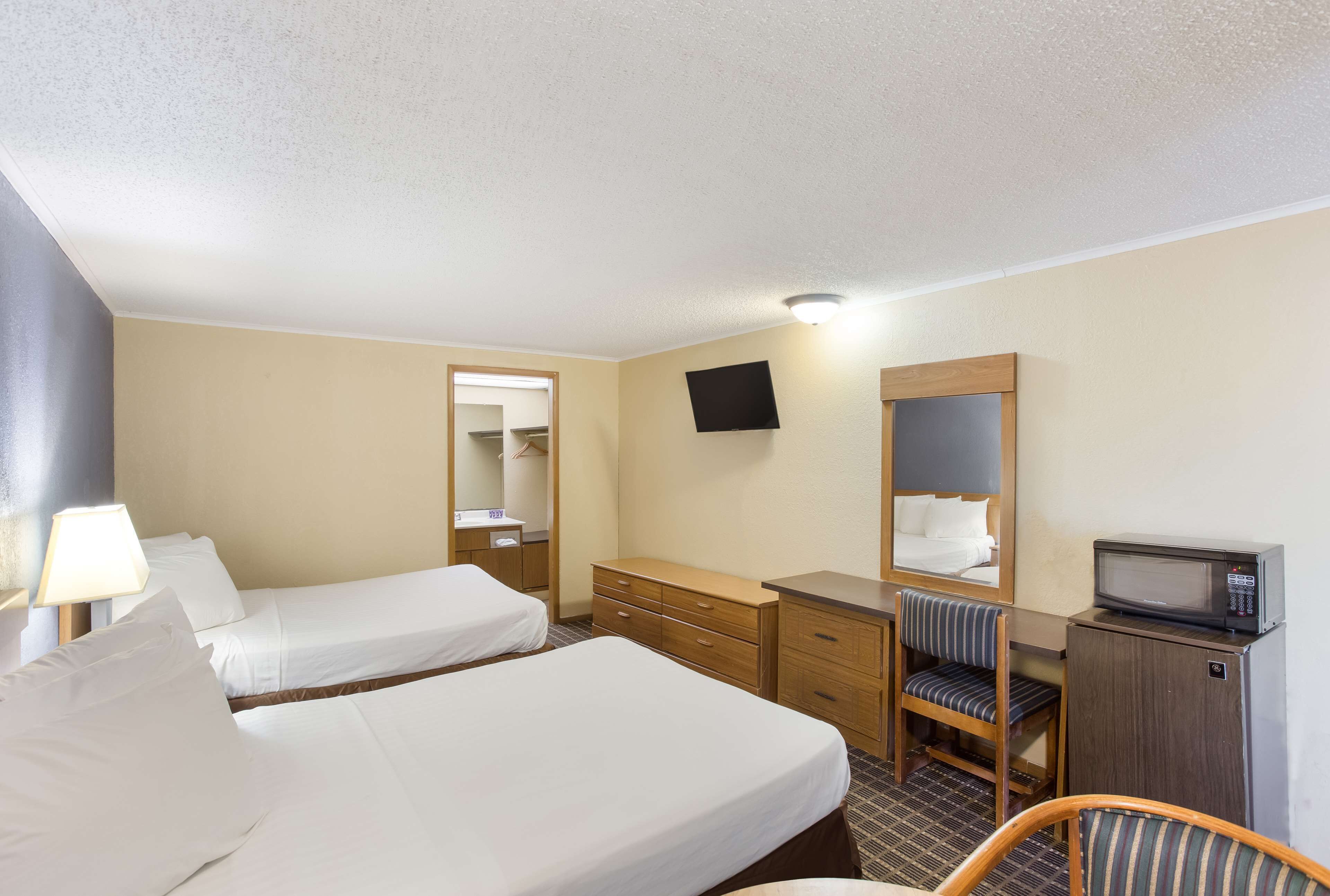 A hotel room with two beds, a desk, a chair, a television, and a microwave.