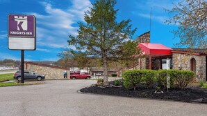 A Knights Inn sign, a stone building with a red roof, and a parking area with two cars. - Knights Inn Ashland (Ashland)