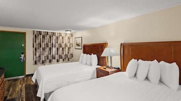 A hotel room with two beds, a green door, a patterned curtain, a wooden headboard, a bedside table with a lamp, and a framed picture on the wall.