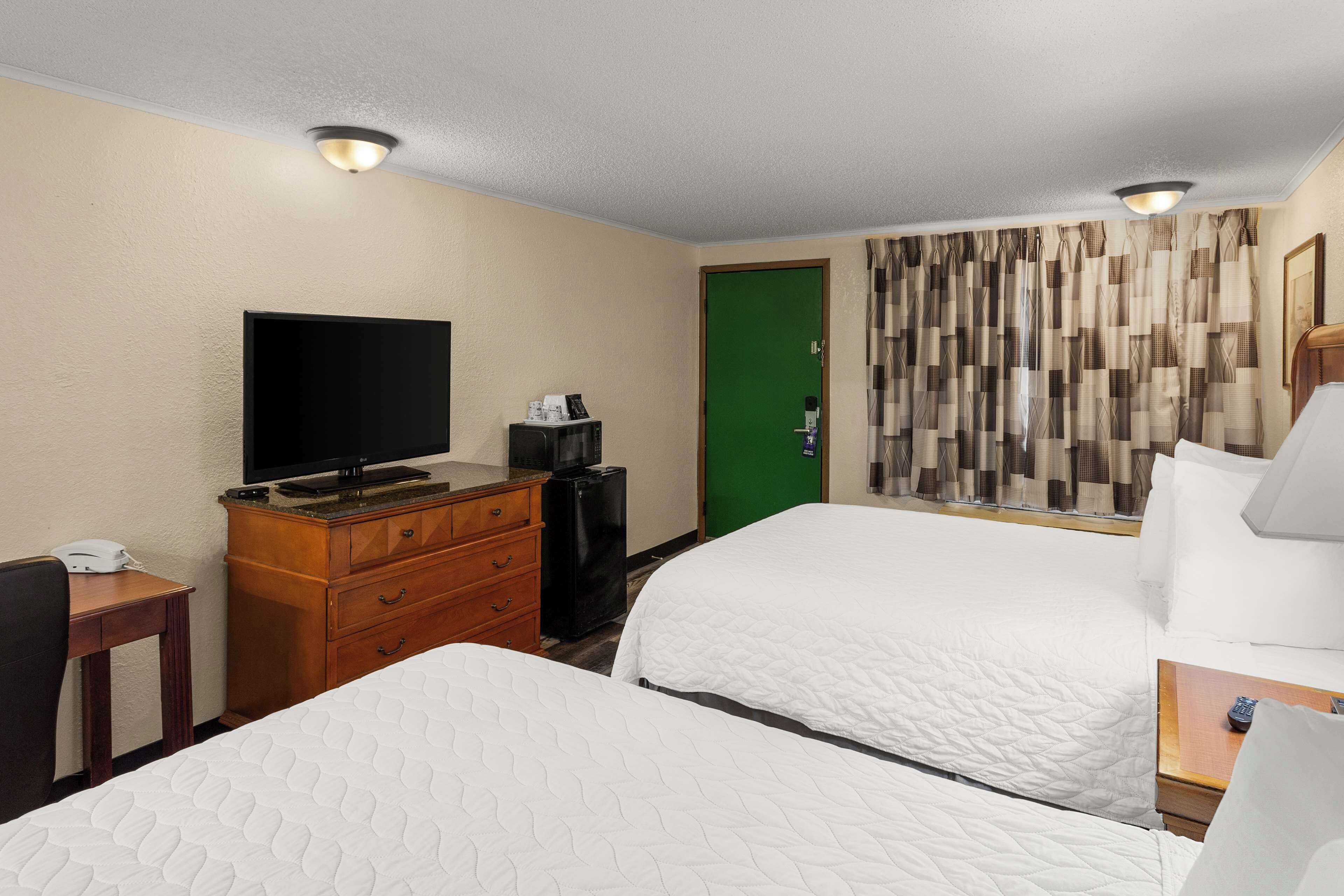 A hotel room with two beds, a television, a dresser, and a green door.