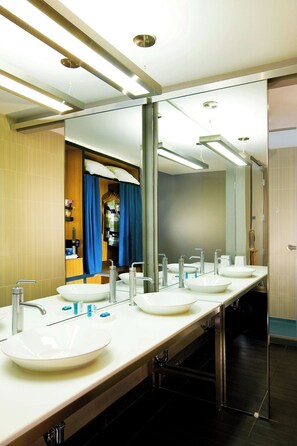 Un baño moderno con tres lavamanos, un espejo grande y una zona de ducha.