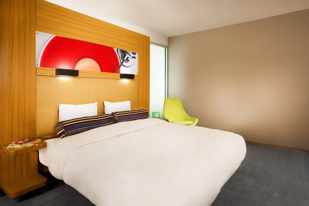 A hotel room with a large bed, a wooden headboard, a bright green chair, and a red accent wall.