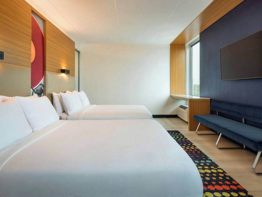 A hotel room with two beds, a TV, a desk, and a window.