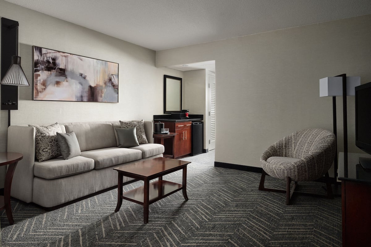 A modern living room with a sofa, coffee table, and armchair, a flat-screen TV, and a painting on the wall.