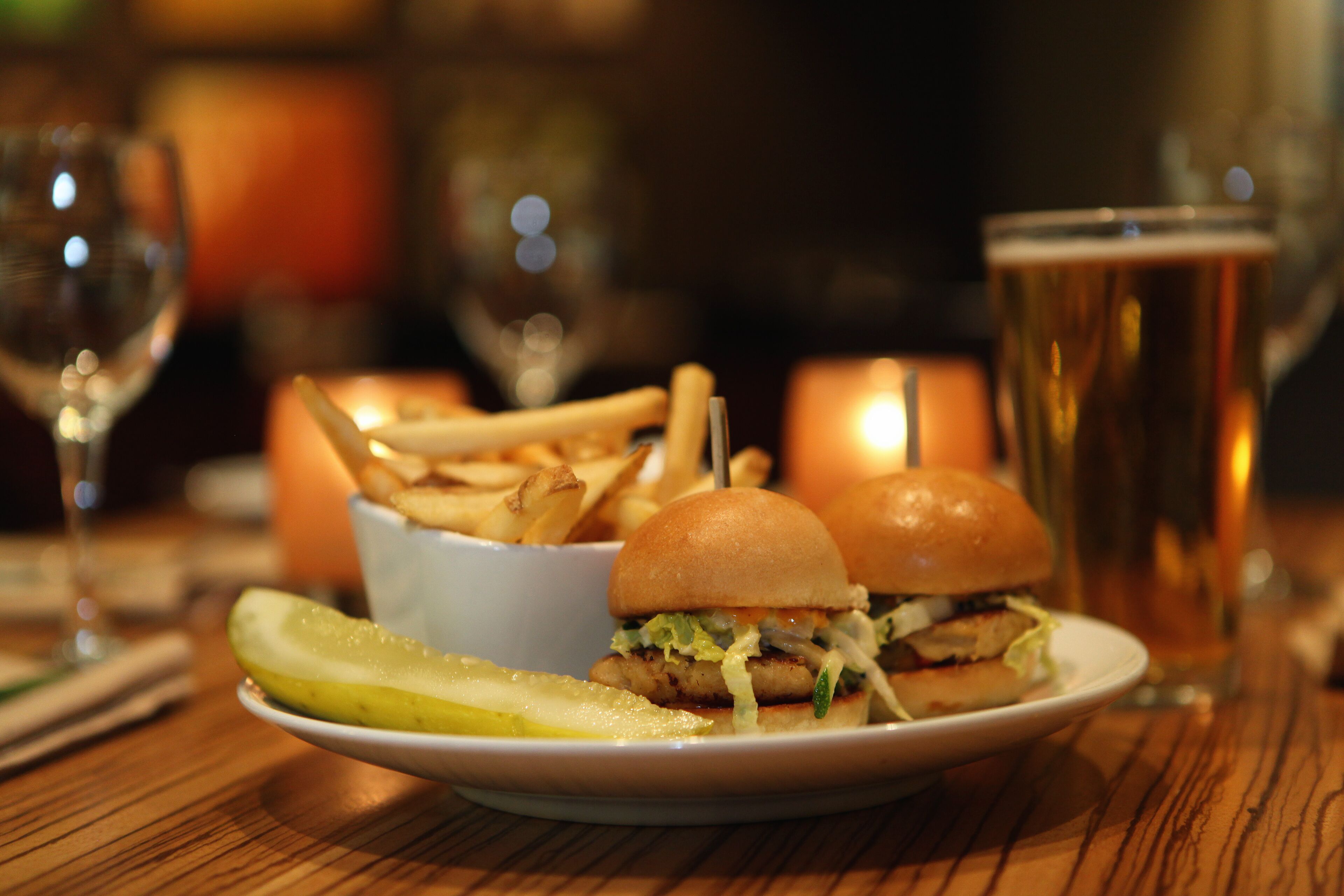 A plate with a burger, fries, and a pickle on a wooden table.