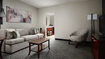 A modern hotel room with a sofa, armchair, coffee table, and a flat-screen TV.