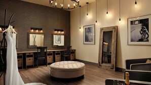 A modern room with a wooden floor, a round ottoman, a desk with chairs, a mirror, and framed pictures on the walls. - Minneapolis Marriott Northwest Hotel & Conference Center (Brooklyn Park)