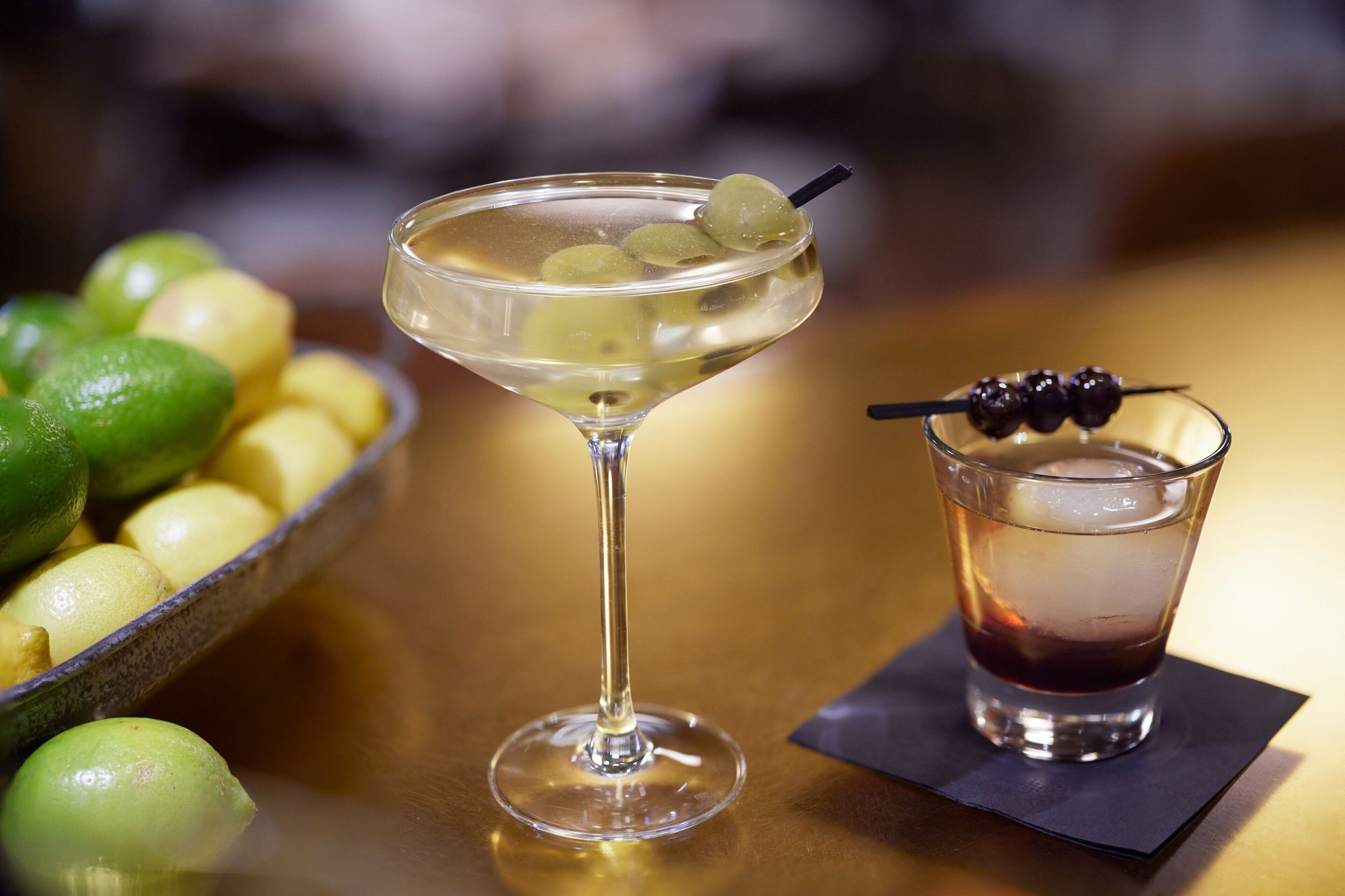 A martini glass with olives and a shot glass with ice cubes on a table.