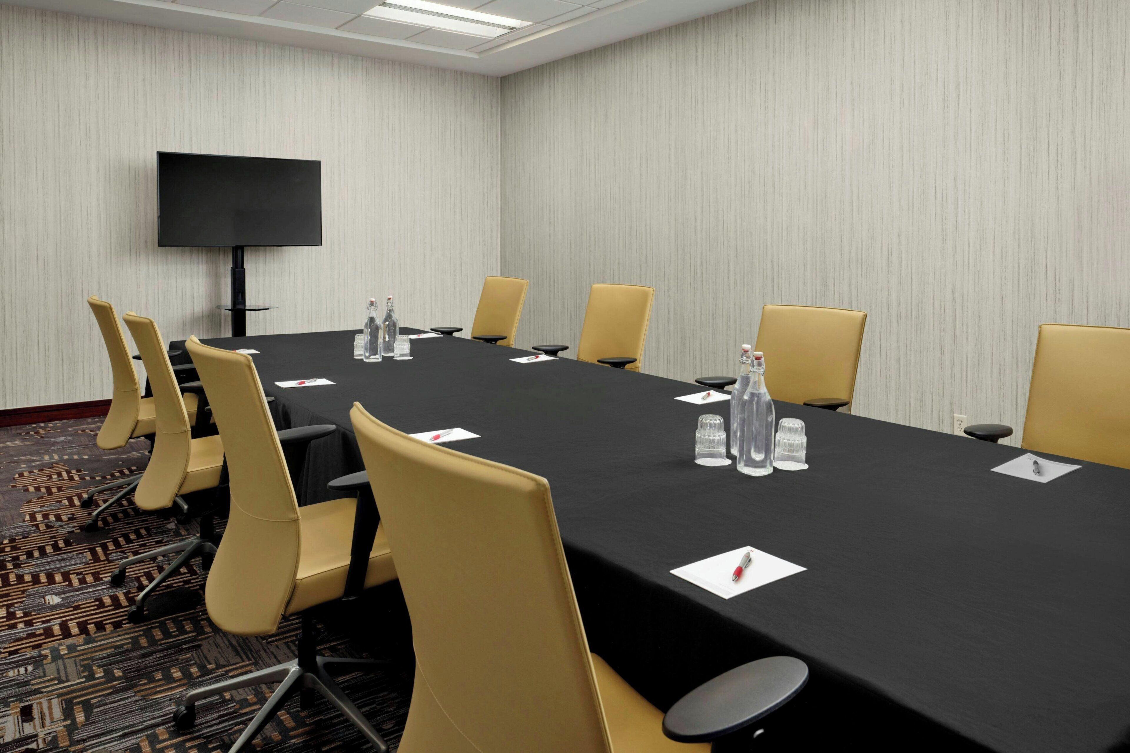 A conference room with a long table, chairs, a TV, and water bottles.