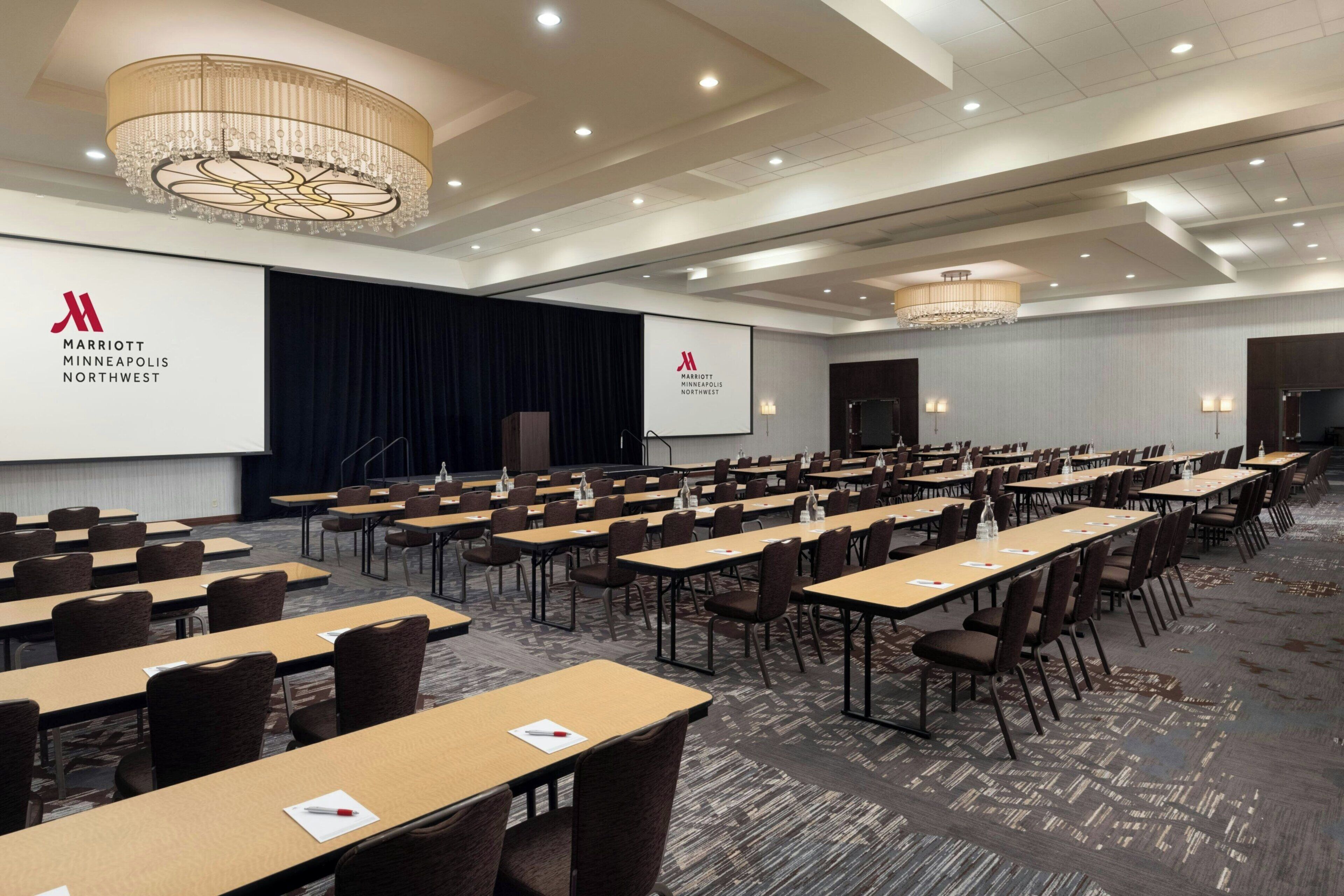 A conference room with rows of tables and chairs, a large screen, and a chandelier.