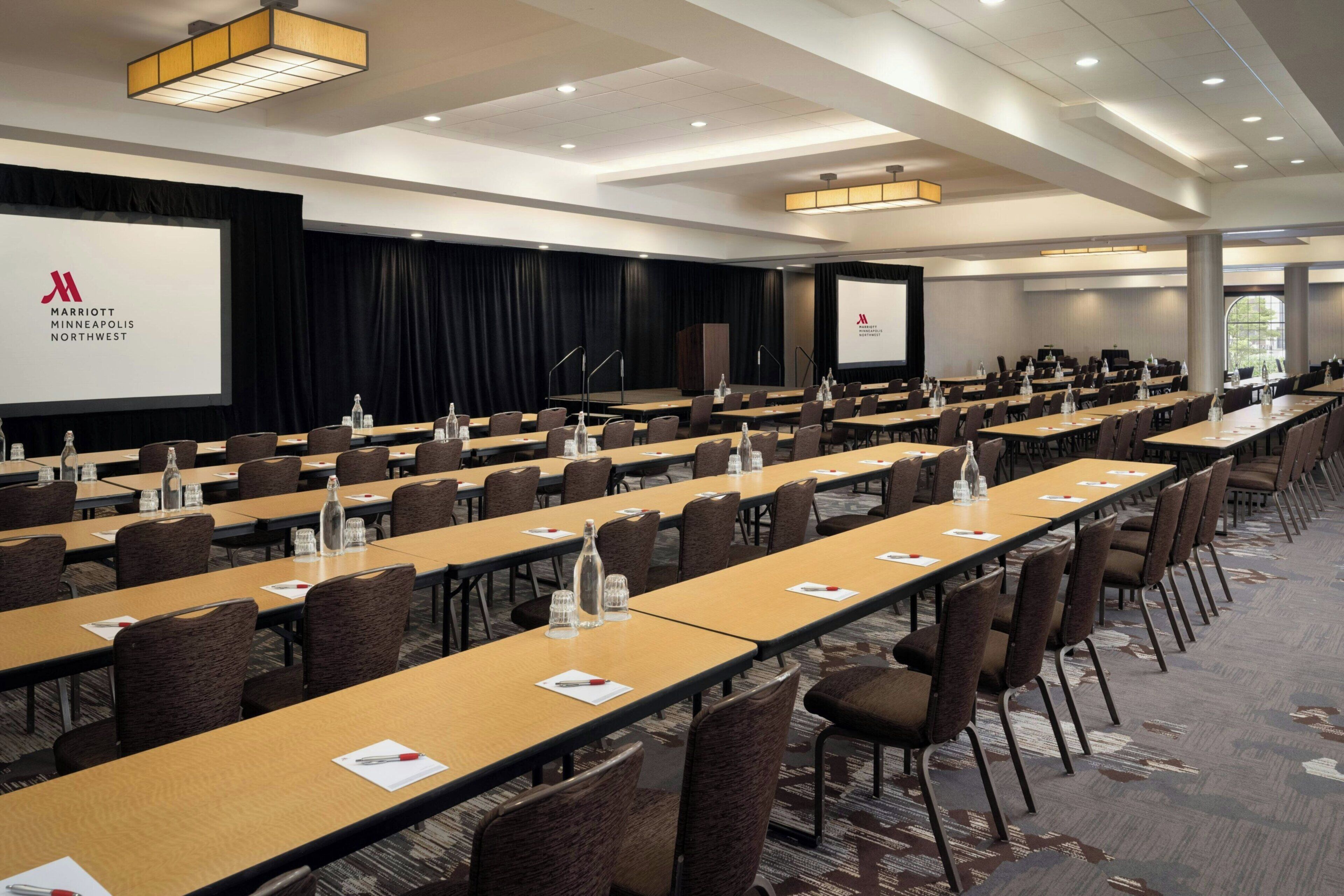 A conference room with long tables, chairs, and a large screen displaying the Marriott Minneapolis Northwest logo.