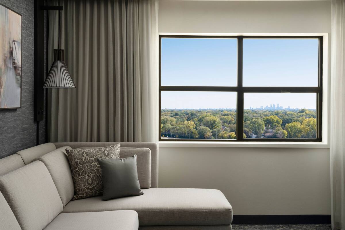 A modern living room with a large window offering a city view, a sofa with patterned cushions, and a pendant light.