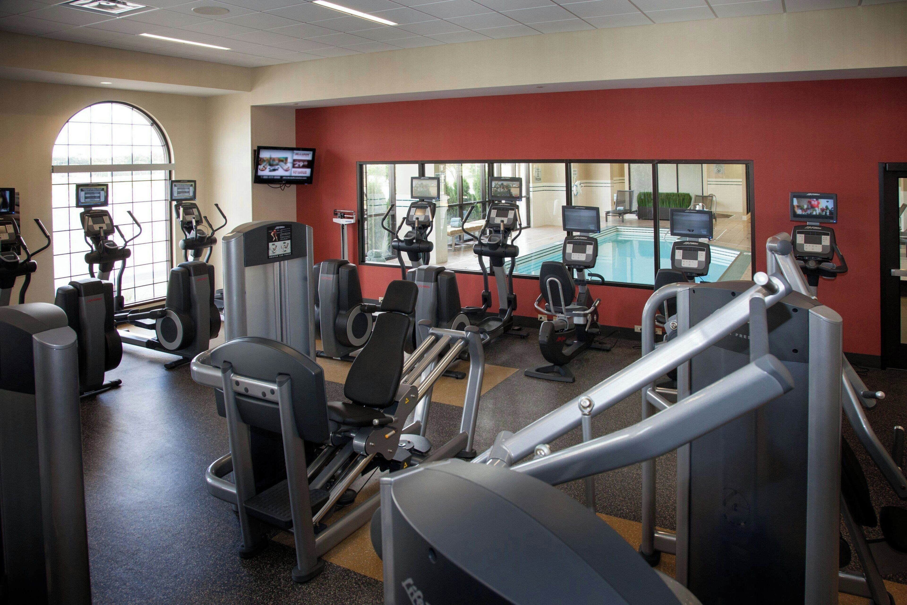 A gym with various exercise machines, a television screen, and a large window.