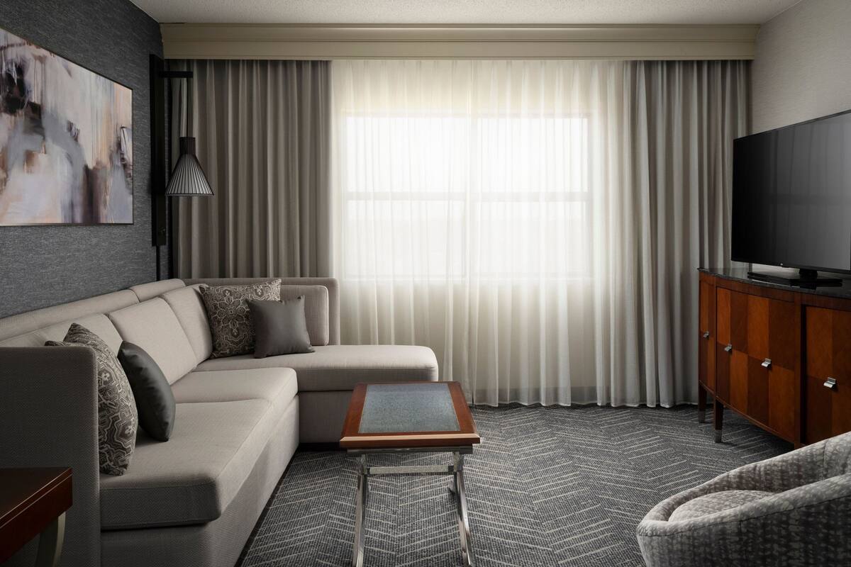 A modern hotel room with a sectional sofa, a small side table, a television, and a cabinet.