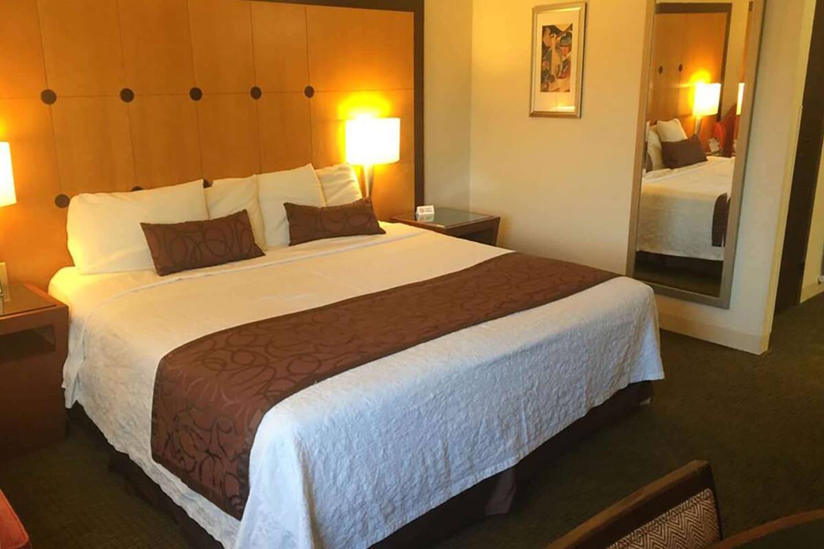 A hotel room with a large bed, two bedside lamps, a nightstand, a mirror, and a framed picture on the wall.
