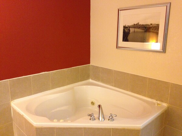 A bathroom with a large bathtub, beige tiles, and a framed picture on the wall.