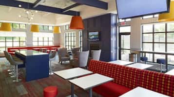 Un interior de restaurante moderno con techos altos, ventanas amplias y una variedad de opciones de asientos, incluyendo mesas y cabinas.