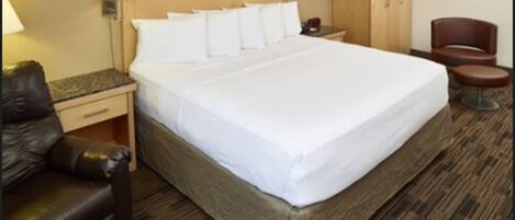 Una habitación de hotel con una cama grande, un cabecero de madera, dos lámparas de noche, un armario de madera, un sillón de cuero y una pequeña mesa redonda.