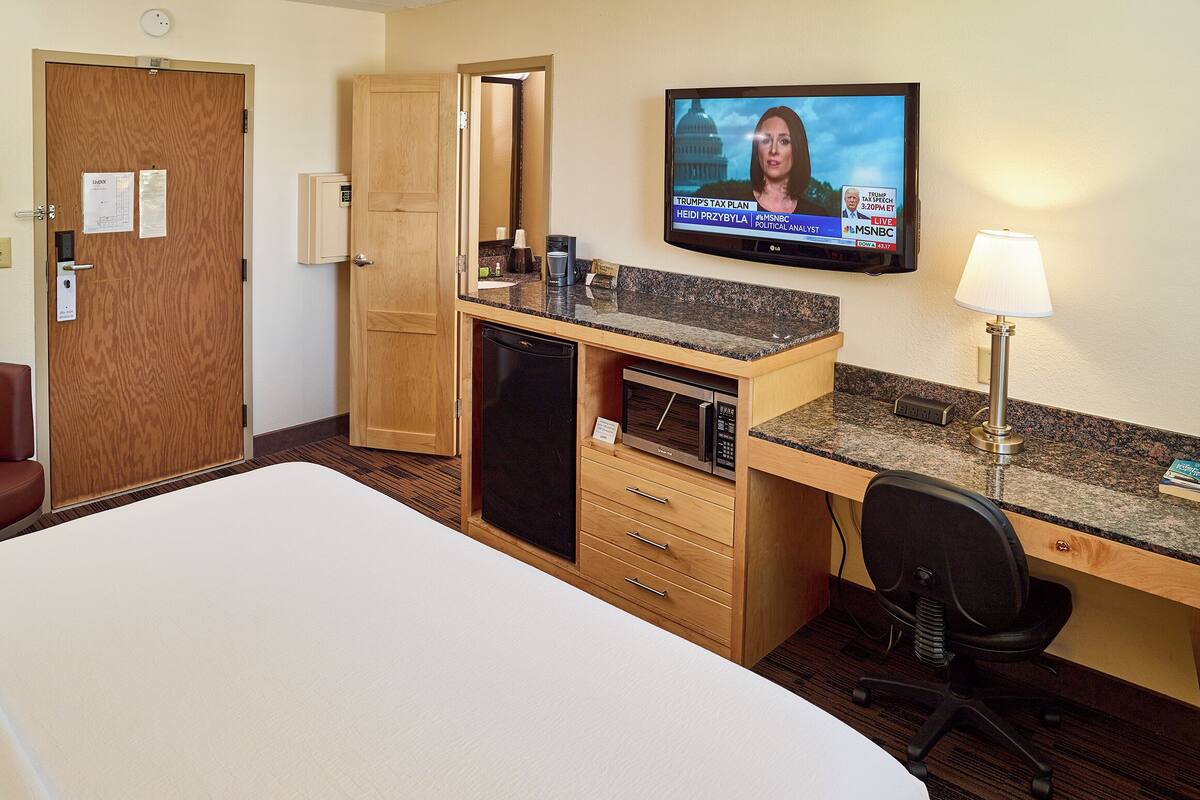A hotel room with a bed, a desk with a computer, a television, and a lamp.