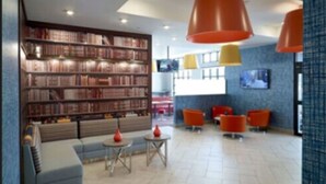 Una biblioteca moderna con estanterías, zonas de descanso y lámparas colgantes naranjas.