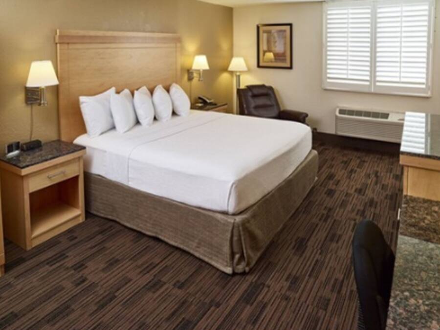 A hotel room with a large bed, two bedside tables with lamps, a chair, a desk, and a window with blinds.