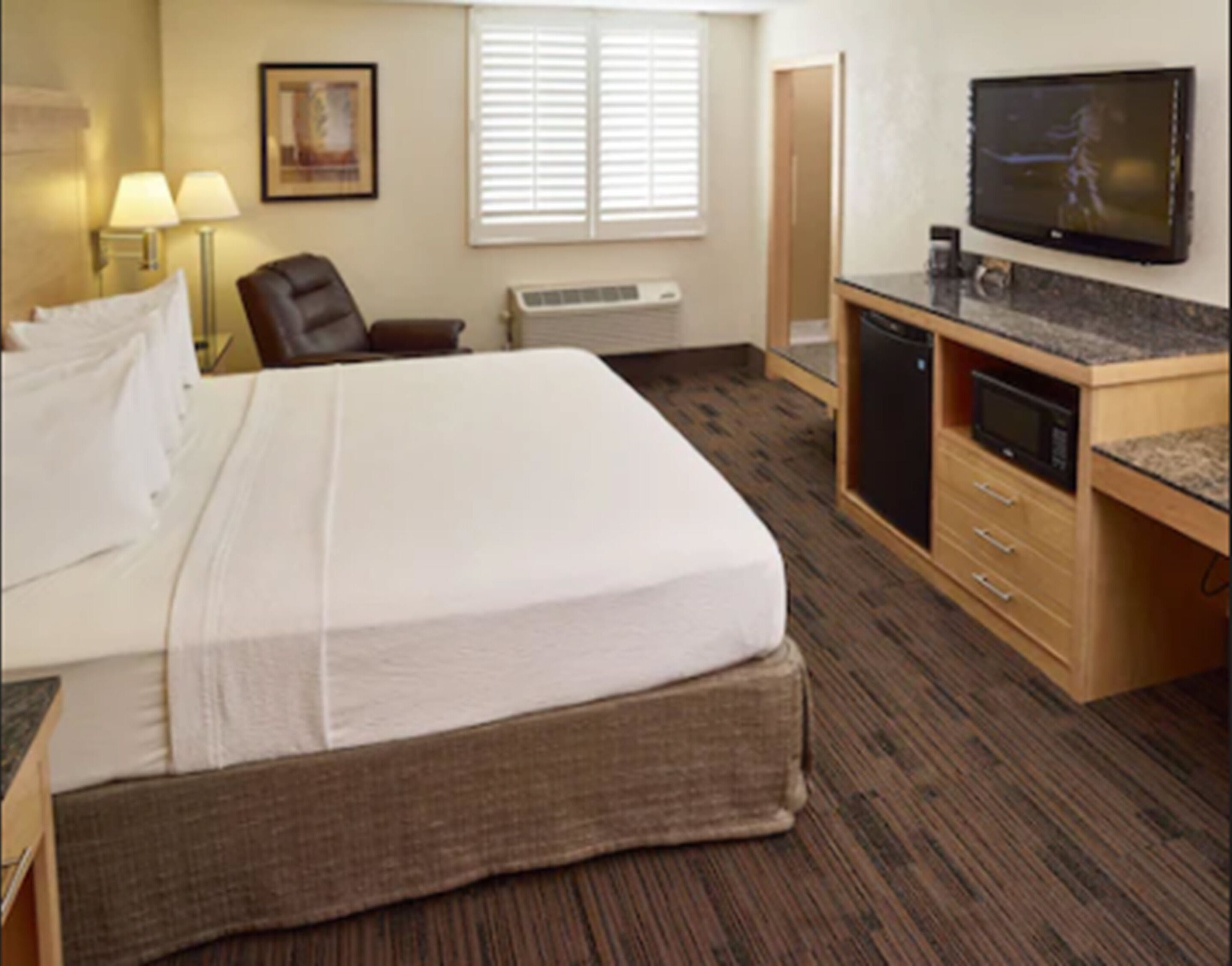 Une chambre d’hôtel avec un grand lit, un bureau équipé d’un micro-ondes, une télévision et une fenêtre avec des stores.