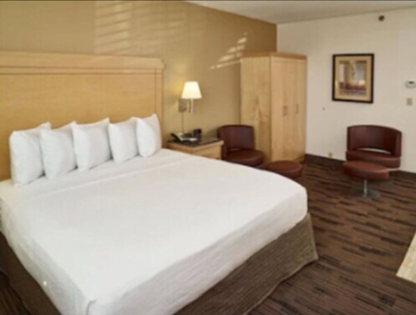 Habitación de hotel con una cama grande, cabecera de madera, escritorio con lámpara, una silla y un armario.