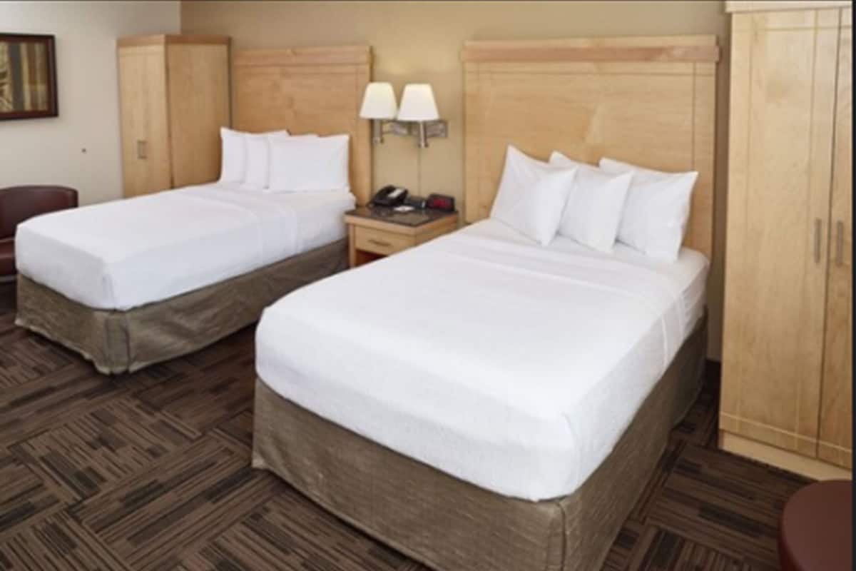 A hotel room with two single beds, a wooden headboard, a nightstand with a lamp, and a wardrobe.