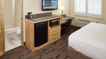 A hotel room with a bed, a desk with a computer, a television, and a small kitchenette.