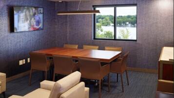 A conference room with a large table and chairs, a television on the wall, and a window with a view of trees.