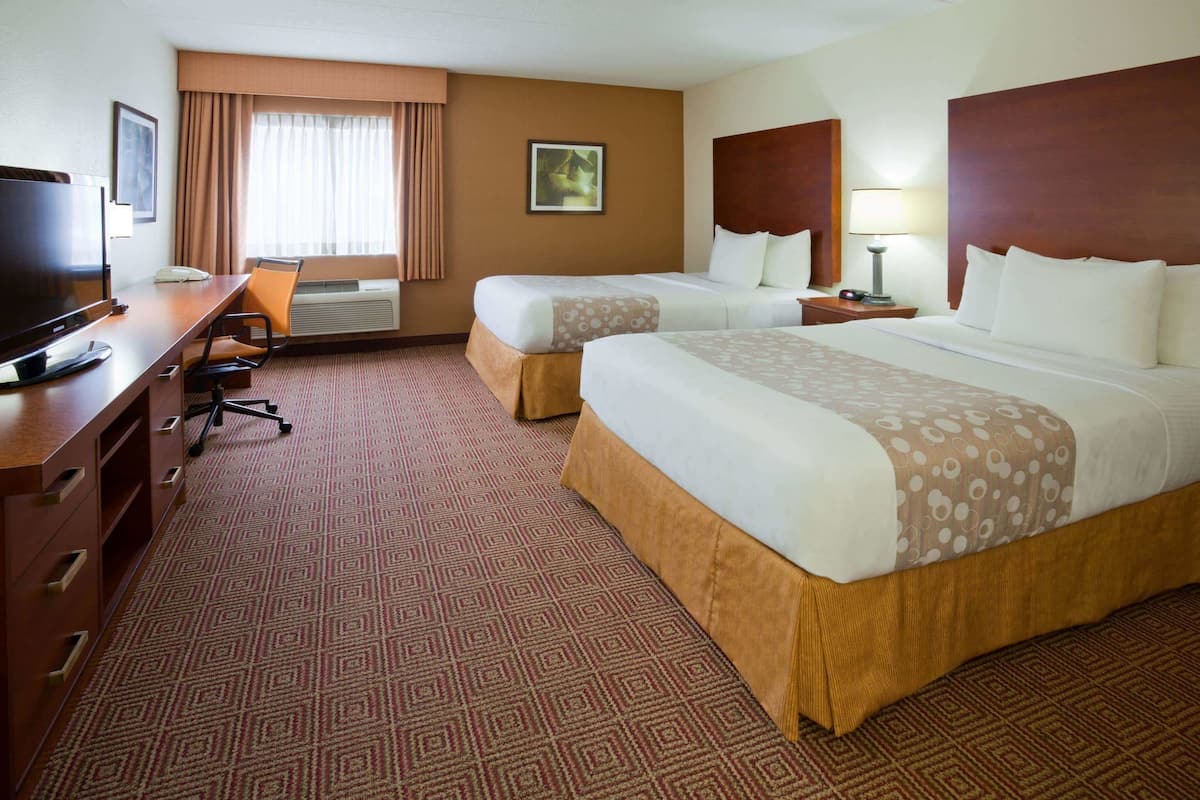A hotel room with two beds, a desk with a television, a chair, and a window with curtains.